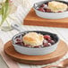 A Valor enameled mini cast iron skillet of fruit cobbler on a wooden tray.