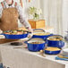A woman wearing an apron holding a blue Valor enameled cast iron dutch oven with food in it.