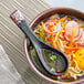 A bowl of ramen with vegetables and an Acopa black stoneware soup spoon.