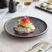 An Acopa Heika black stoneware plate with food on it on a table.