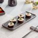 A rectangular Acopa black stoneware plate with sushi on a table.