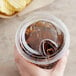 A hand using a Choice clear plastic sip-through lid on a plastic cup with a drink in it.