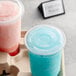 Choice clear plastic lids on two plastic cups filled with pink and blue frozen drinks on a tray.