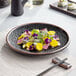 A black Acopa Heika stoneware plate with sushi and chopsticks on it.