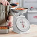 A person weighing food in a metal bowl on a Galaxy portion scale.