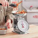 A woman using a Galaxy portion scale to weigh food in a stainless steel bowl.