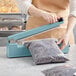 A person using a Thunder Group manual impulse bag sealer to seal a bag of beans.