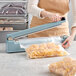 A woman using a Thunder Group manual impulse bag sealer on a plastic bag of pasta.