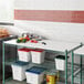 A white Regency Polyethylene cutting board on a wire shelf above food.