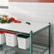 A white Regency Polyethylene cutting board on a wire shelf above a white container with a red lid.