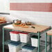 A Regency hardwood cutting board insert on a green wire shelf above food containers.