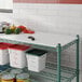 A white Regency Polyethylene cutting board on a green wire shelf over cans of food.