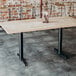 A NOROCK sandstone black powder-coated steel table base on a wood table with a metal basket of utensils on it.