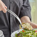 A person using a Vollrath stainless steel oval serving spoon to serve food from a bowl on a table.