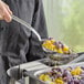 A person using a Vollrath stainless steel slotted oval serving spoon to serve food