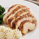 A white plate with a slice of Lawry's Garlic Pepper chicken and mashed potatoes with broccoli.