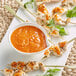A plate of food with sauce and chicken skewers next to a bowl of orange soup.