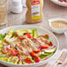A bowl of salad with lettuce, chicken, and Zatarain's Creole Mustard on a table.