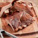 A piece of meat on a wooden cutting board with a knife and Lawry's Pit BBQ Seasoning.