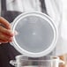 A person holding a plastic lid over a clear container.