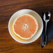 A Homer Laughlin bright white china bowl with a spoon and half of a grapefruit on a table.