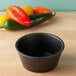 A black HS Inc. polyethylene ramekin on a wood table next to red peppers.