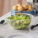 A clear plastic round catering bowl filled with salad on a table.