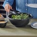 A woman pouring salad into a Visions black plastic bowl.