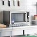 An Amana medium volume stainless steel commercial microwave on a counter.