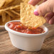 A person holding a chip dips it into a bowl of salsa.