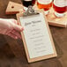 A hand holding a Choice hardback menu on a clipboard next to a glass of beer.