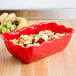 A red Cambro deli crock filled with fruit on a table.