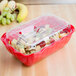 A red Cambro deli crock with fruit inside.