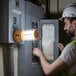 A man in a hard hat using a Voltec Rechargeable Portable LED Work Light on a machine.