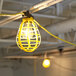 A light bulb in a yellow cage on a wire with a plug.