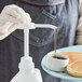 A person using a white Tablecraft condiment pump to pour syrup over a dish of pancakes.
