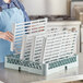 A woman holding a Regency green epoxy polymer wire shelving kit with white plastic panels.