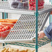 A person standing near a Regency green epoxy wire shelf with food on it.