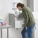 A woman standing next to a Regency wall mounted hands-free hand sink.