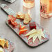 An American Metalcraft rectangular faux reclaimed wood melamine serving board with different types of cheese on it.