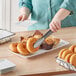 A person cutting doughnuts on an American Metalcraft white rectangular melamine tray.
