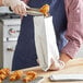 A person in a blue apron holding a Carnival King foil bag of fried chicken.