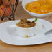 A white bowl of peaches on a table with a metal spoon.