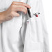 A person in a white Uncommon Chef Aruba Pro Vent chef coat putting a pen in the pocket.