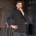 A man wearing a Uncommon Chef black chef coat with red piping.