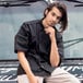 A man leaning on a counter in a food truck interior wearing a black Uncommon Chef Delray Pro Vent short sleeve chef coat with a mesh back.