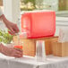A person pouring orange juice into a clear plastic beverage dispenser.
