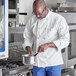 A man in a white Uncommon Chef long sleeve coat cooking in a kitchen.