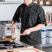 A black short sleeve chef coat with a mesh back, worn by a person cooking in a kitchen.