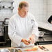 A man in a Uncommon Chef white long sleeve chef coat preparing food.